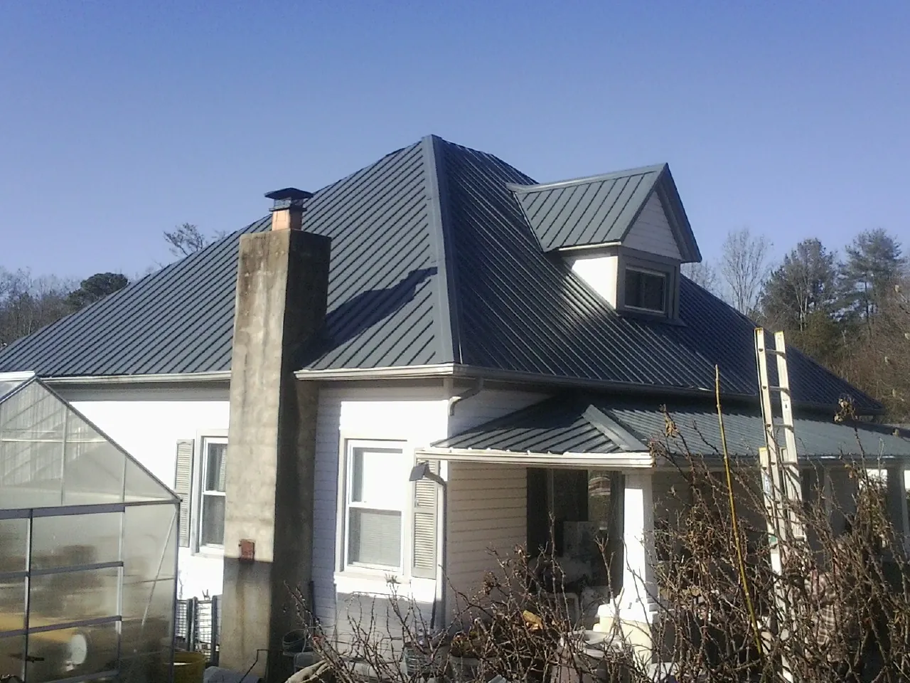Dark blue standing seam metal roof on a white farmhouse with dormer — Slate & Tile Roof Repair by Roofing Brothers in Pointblank