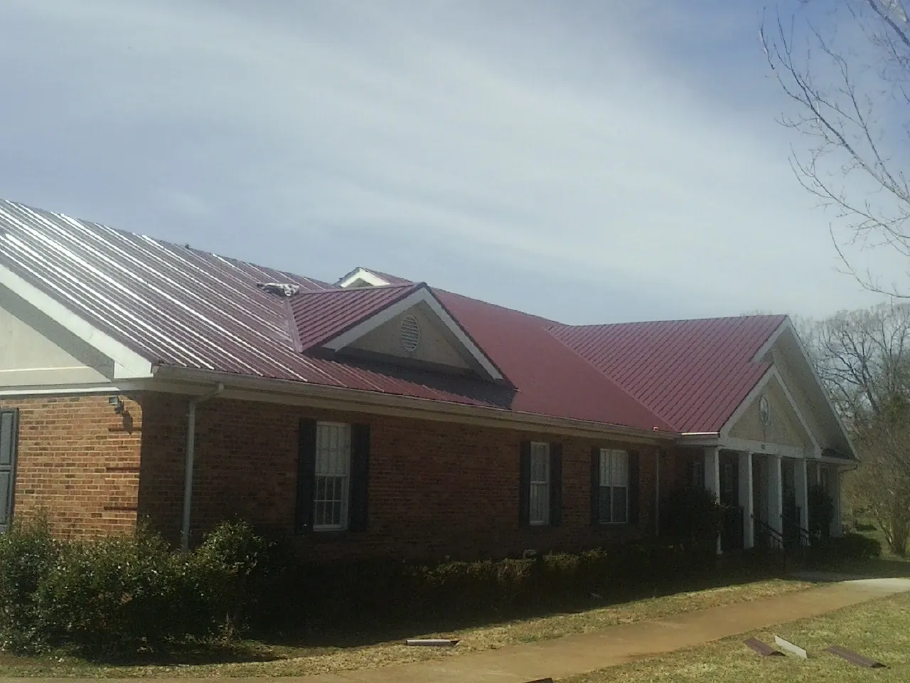 Red metal roof with gabled entries on a long brick building, from a Hail Damage Roof Repair job in Pointblank