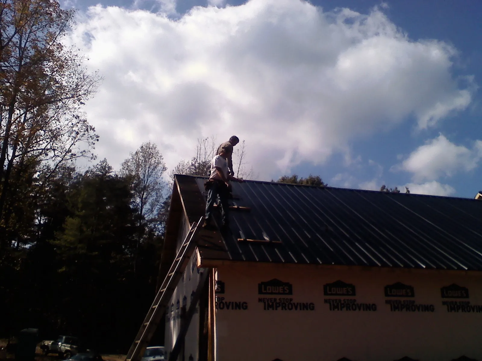 Roofer fastening dark metal panels high against a cloudy sky, from a Roof Inspection job in Pointblank